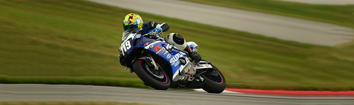 A rider turning a tight corner on a sports bike on a race track with grass in the background. 